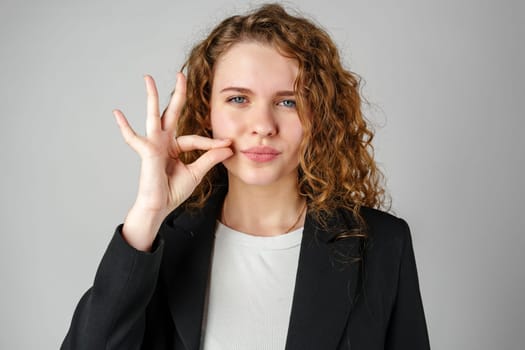 Young Woman Gesturing Silence With Finger on Lips Against a Grey Background close up