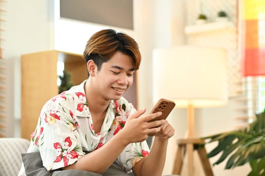 Smiling relaxed young man texting messaging on smartphone or doing shopping online.