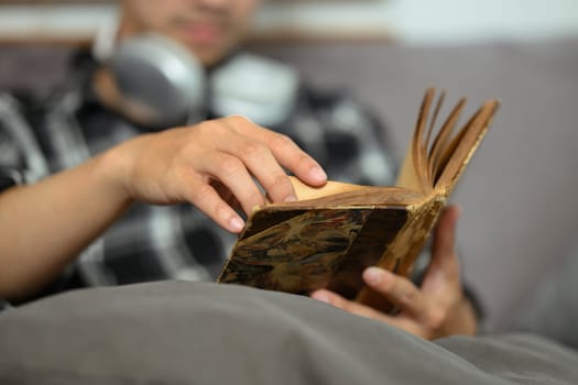 Man relaxing on couch in living room and reading book. Hobby, leisure and knowledge concept.