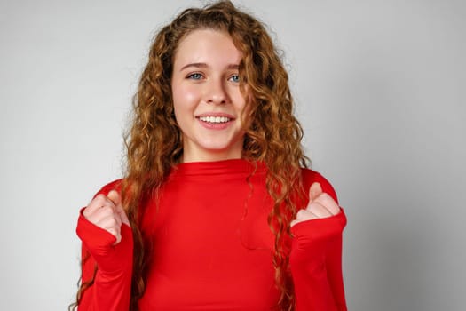 Excited Young Woman Celebrates Success With Raised Fists Against a Gray Background in studio