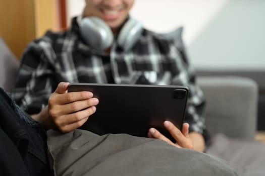 Cropped shot of man watching video using digital tablet and relaxing on couch in living room.