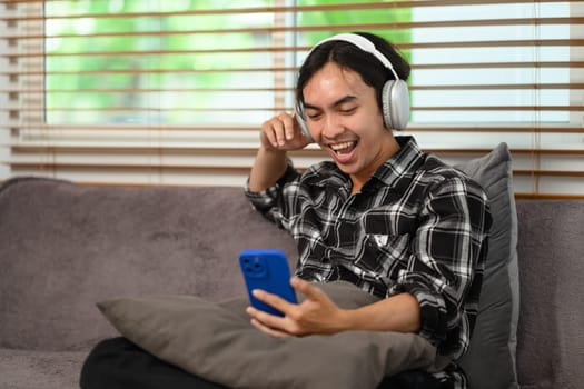 Happy asian man with headphones enjoying his favorite music playlist on mobile phone.