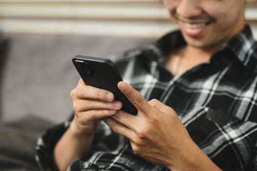 Smiling adult man texting message, chatting in mobile apps while sitting on couch at home.