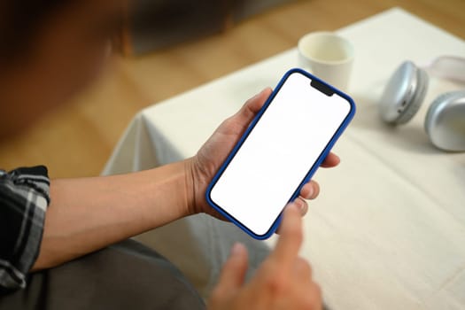 Cropped shot of man's hand holding smartphone with blank screen sitting on couple in living room.