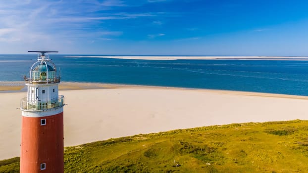 A picturesque scene unfolds as a towering lighthouse stands tall on the sandy shores of Texel, Netherlands, casting its guiding light over the vast beach.