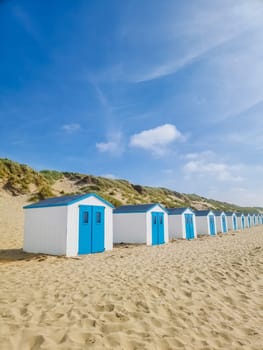 A vibrant row of colorful beach huts lines the sandy beach of Texel, Netherlands, creating a picturesque scene against the backdrop of the ocean.