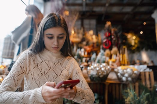 A captivating, colorful girl admiring Christmas decor and browsing her smartphone. High quality photo