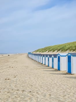 A vibrant row of beach huts line the sandy beach under a clear blue sky, adding a splash of color to the serene seascape.