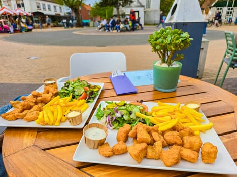 Two plates of golden-battered fish and crispy chips laid out on a rustic wooden table by the sea on Texel island.