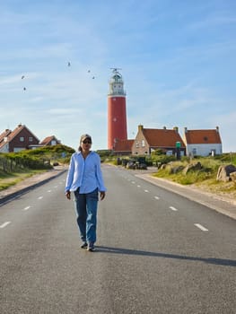 A lone man walks down an empty road towards a distant lighthouse in Texel, Netherlands.