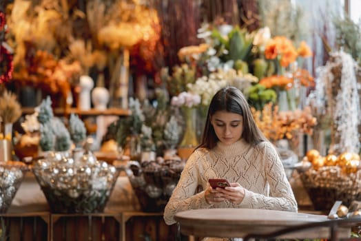 A beautiful, vibrant girl with a smartphone in hand at the Christmas decor store. High quality photo