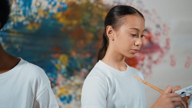 Multicultural student paint the canvas together in art lesson with colorful stained wall. Closeup of african boy and caucasian girl drawing picture or doing creative activity together. Edification.