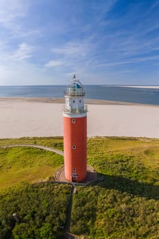 A breathtaking aerial view of a solitary lighthouse standing tall on the sandy beach, casting its light out to sea, guiding ships safely to shore. The iconic red lighthouse of Texel Netherlands