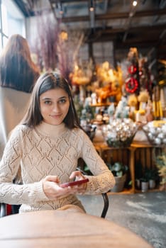 A beautiful, vibrant girl with a smartphone in hand at the Christmas decor store. High quality photo