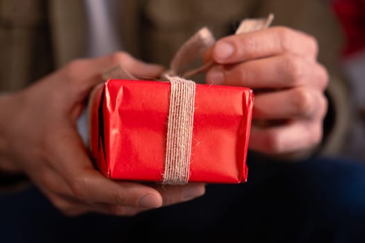 Elegant man holding gift with ribbon on the sofa at home.Celebrating Valentine's Day