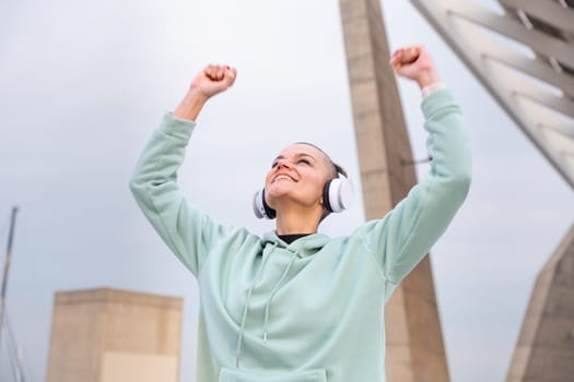 Happy fit woman smiling with sports headphones, celebrating race victory with arms raised.