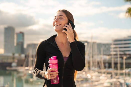 cheerful young woman talking on smartphone and holding sport bottle.