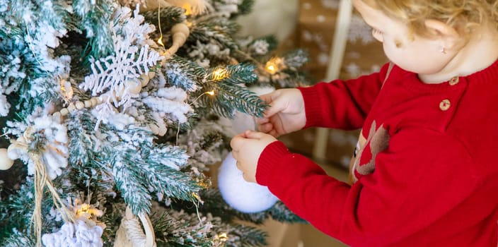 The child hangs a decoration on the Christmas tree. Selective focus. Kid.