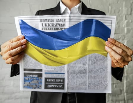 Hand holding a newspaper with the drawing of the flag of Ukraine on a white background