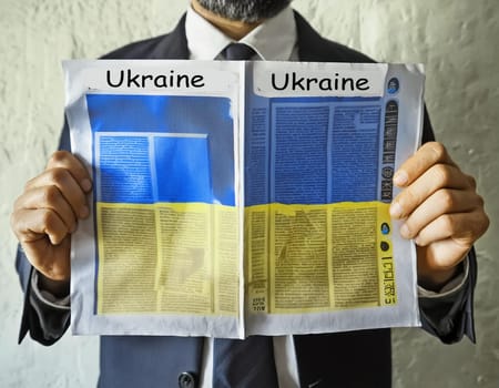 Hand holding a newspaper with the drawing of the flag of Ukraine on a white background