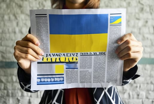 Hand holding a newspaper with the drawing of the flag of Ukraine on a white background