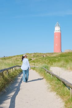 A woman peacefully walks along a winding path near the majestic Texel Lighthouse, taking in the serene surroundings. The iconic red lighthouse of Texel Netherlands