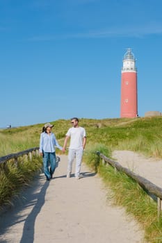 A couple leisurely walks along a path near a picturesque lighthouse in Texel, Netherlands, enjoying the scenic views and each others company. The iconic red lighthouse of Texel Netherlands