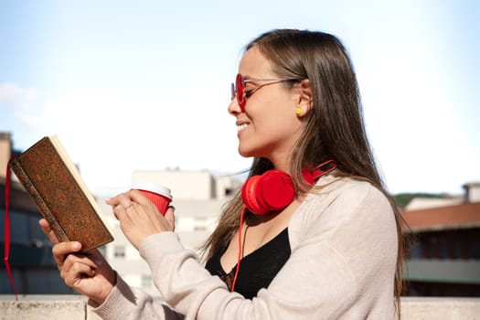 A concentrated Caucasian woman reads a book while drinking coffee.