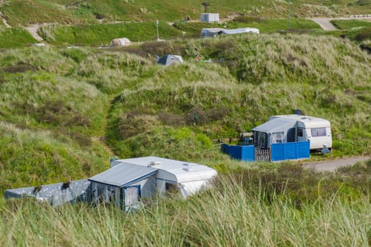 A serene scene where a group of RVs are peacefully parked on a grassy hillside in Texel, Netherlands, blending harmoniously with the natural beauty surrounding them.