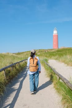 A woman leisurely walks down a serene path near the iconic Texel lighthouse, surrounded by picturesque coastal scenery. The iconic red lighthouse of Texel Netherlands