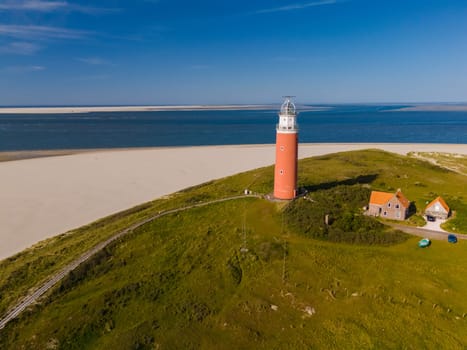 A breathtaking aerial view capturing the towering lighthouse standing tall on the sandy shores of Texel, Netherlands, guiding ships with its radiant light.