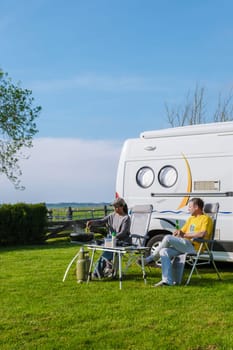 Two individuals sit outside a camper van, surrounded by lush green grass in Texel, Netherlands. They appear relaxed and content, enjoying the peaceful outdoor setting.