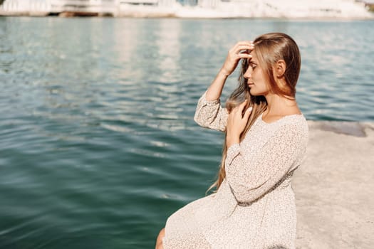 A woman is sitting in the water wearing a white dress. The water is calm and blue. The woman is enjoying the moment and taking in the beauty of the scene