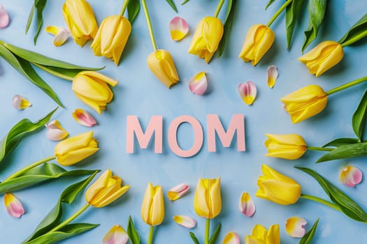 Mother's Day: Flat lay composition with word Mom and yellow tulips on blue background