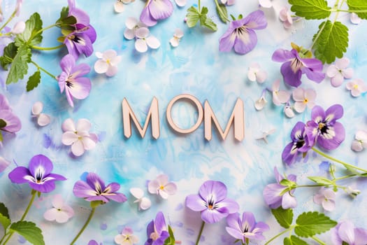 Mother's Day: Word mom made of wooden letters and spring flowers on blue paper background