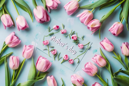 Mother's Day: pink tulips and greeting card on blue background, flat lay