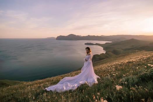 A woman in a white dress stands on a hill overlooking the ocean. The scene is serene and peaceful, with the woman's dress flowing in the wind