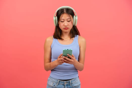 Portrait of angry girl looking at mobile phone, serious, texting on pink background. Concept of human emotions, facial expression. Copy space for your ad