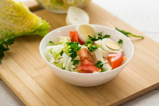 fresh vegetable salad, cabbage, tomatoes in a bowl on a wooden table .