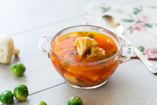 vegetable soup with Brussels sprouts and cauliflower, in a glass plate on a wooden table .