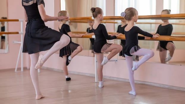 Caucasian woman teaches little girls ballet at the barre