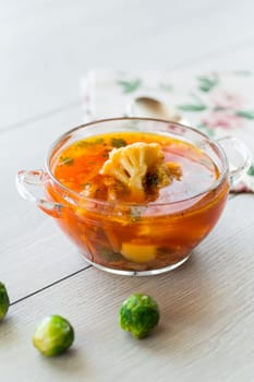 vegetable soup with Brussels sprouts and cauliflower, in a glass plate on a wooden table .