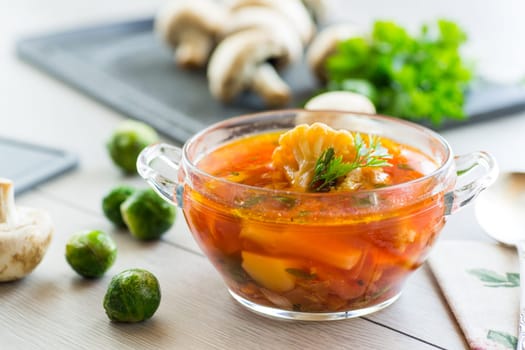 vegetable soup with Brussels sprouts and cauliflower, in a glass plate on a wooden table .