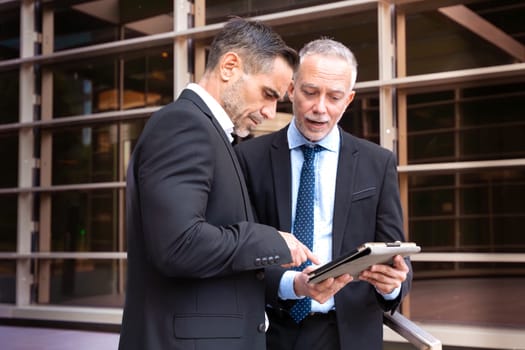 Two trusted business colleagues dressed in formal attire with a digital tablet in hand observing the results of the work done