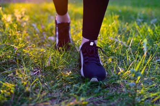 Woman's legs in black leggings and black sneakers on nature background walking on grass