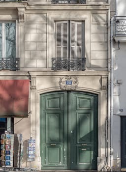 France, Paris - Jan 03, 2024 - Entrance of old building with green wood door and white wooden shutters with balcony on top of building. Classical architecture of building in Paris, Antique building exterior, French street facades, Space for text, Selective focus.