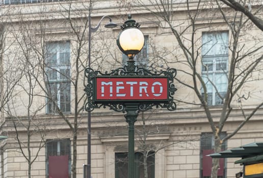 France, Paris - Jan 04, 2024 - A pole with traditional metro sign under lamp in front of classic european building. Signs for the Paris Metro or Entrance to the Metropolitain station, Word "METRO" designed in Art Nouveau and Art deco, Space for text, Selective focus.