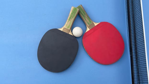 Two table tennis rackets and balls on a blue table with net. High quality photo