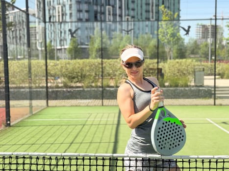 Portrait of active emotional woman playing padel tennis on open court in summer, swinging racket to return ball over net .. High quality photo