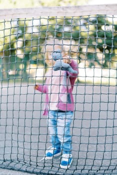 Little girl applies a soft toy to the net while standing behind it on the playground. High quality photo